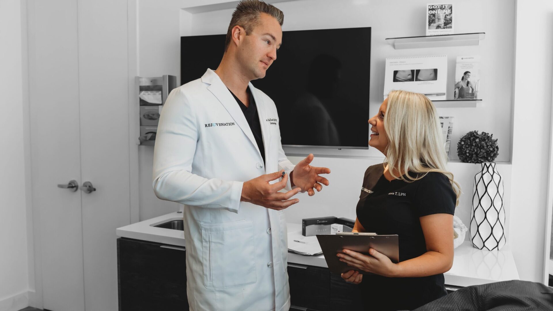 A medical director specializing in dermatology is pictured alongside one of his employees. They are engaged in discussion, reviewing patient cases and discussing clinic operations. 